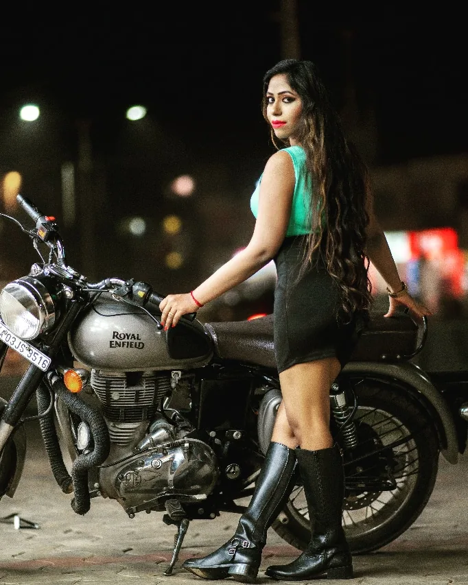 Nibedita beside a Royal Enfield motorcycle on a city street at night