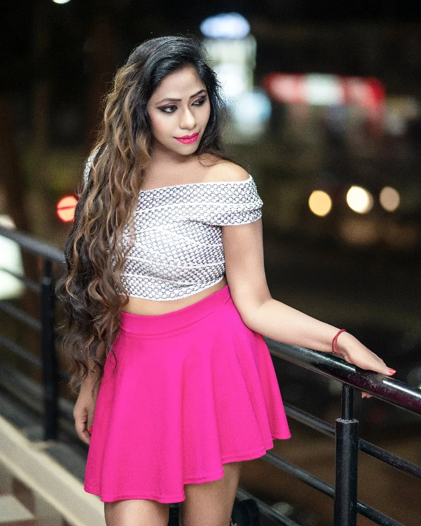 Nibedita in a monochrome crop top and pink skirt at a night shoot, looking over her shoulder